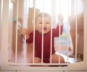 baby sitting behind a baby gate in the doorway